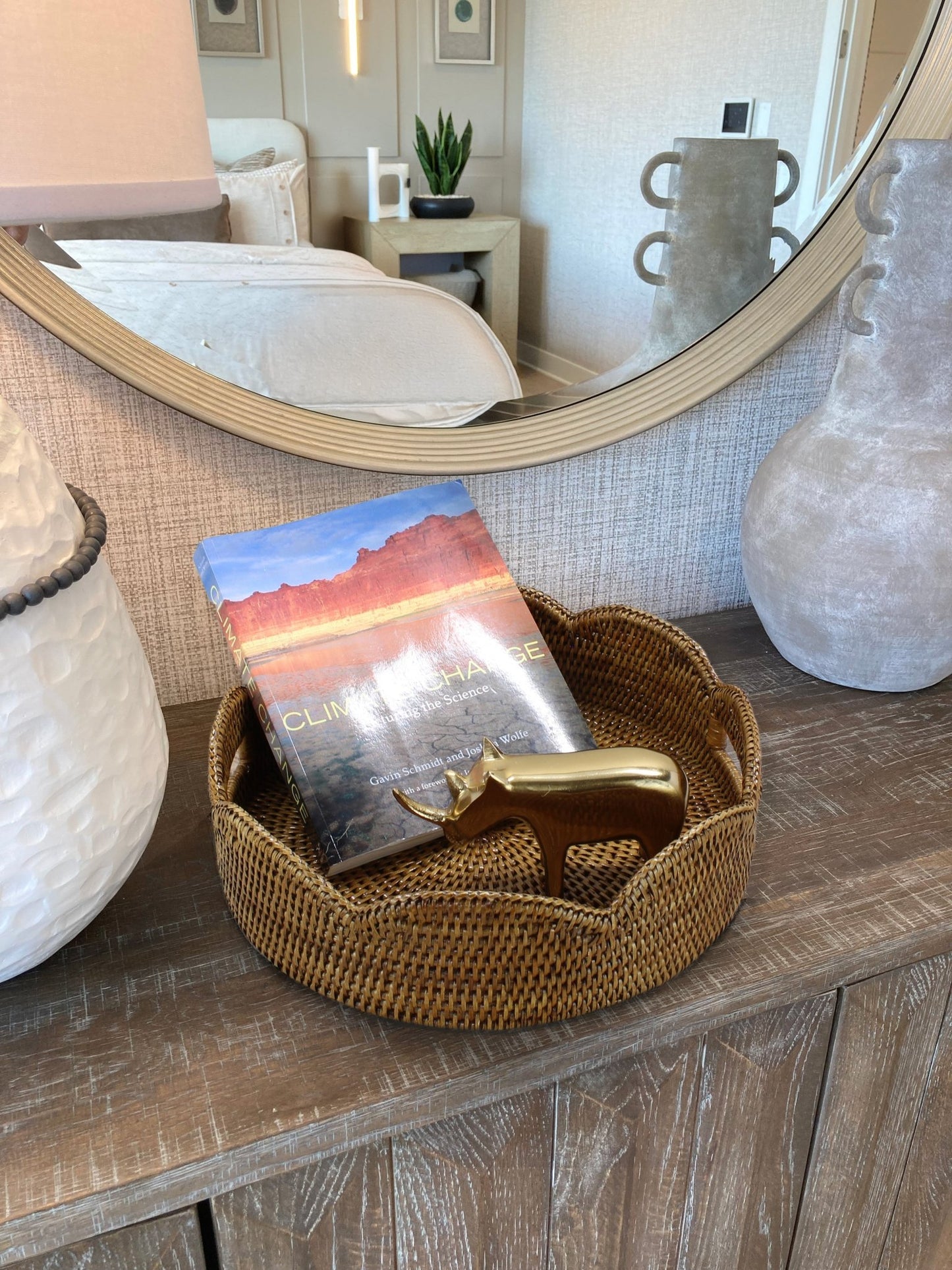Honey brown scalloped round rattan tray styled on bedroom dresser with climate change book and gold rhino figurine for elegant home decor.