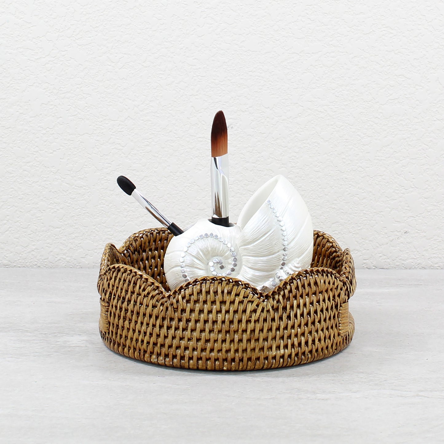 Honey brown scalloped rattan tray with white seashell holder and makeup brushes, perfect for bathroom vanity storage.