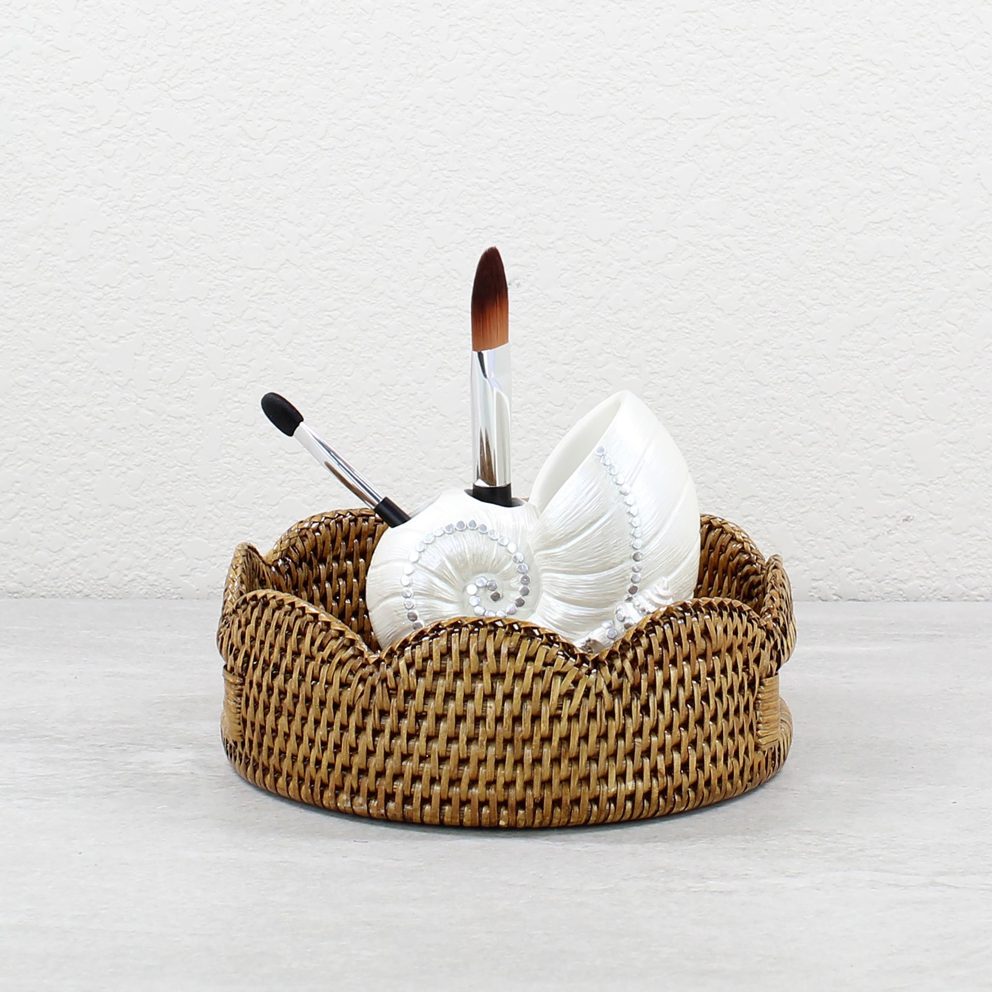 Honey brown scalloped rattan tray with white seashell holder and makeup brushes, perfect for bathroom vanity storage.