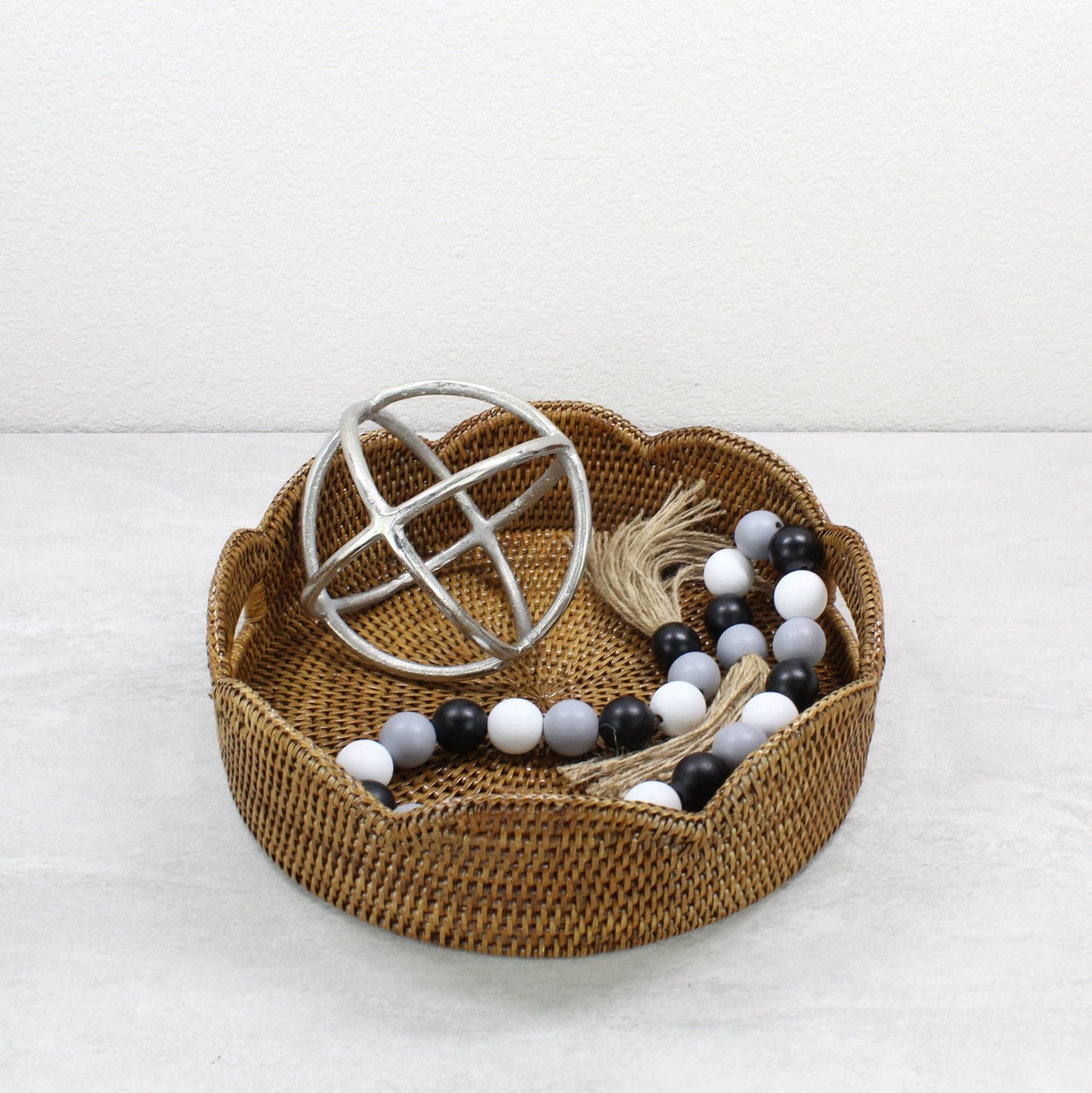 Honey brown scalloped rattan tray with farmhouse beaded garland and silver orb accent, styled for modern rustic home decor.