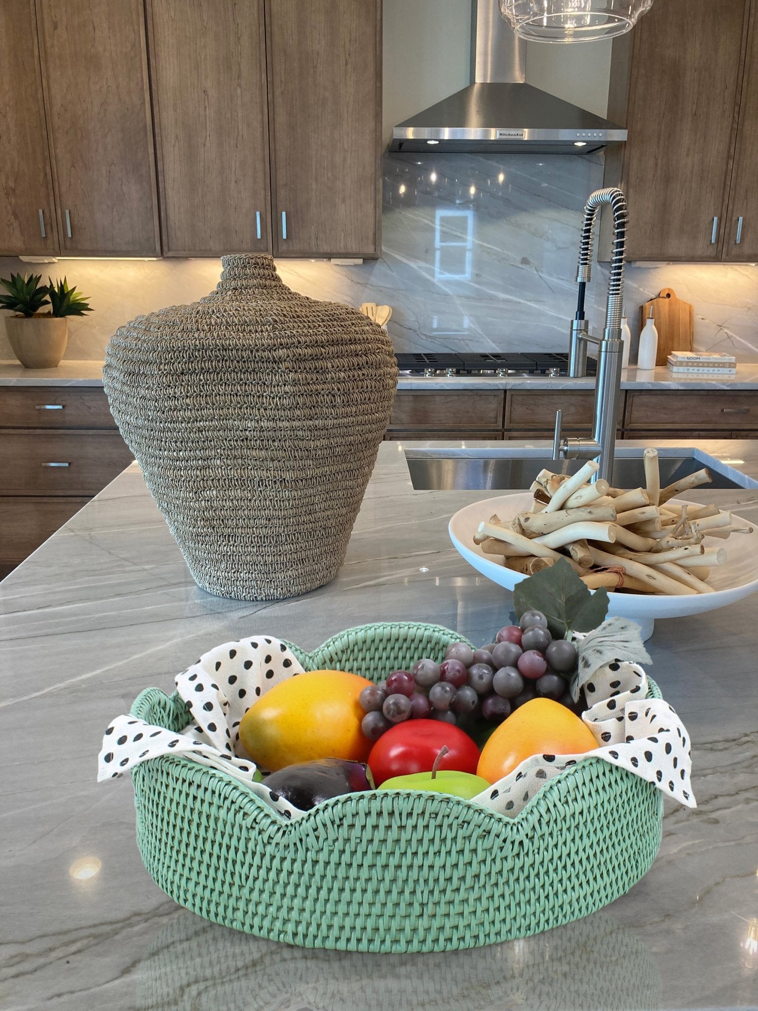 Sage leaf green scalloped round rattan tray on marble kitchen island filled with fresh fruit and cloth liner for serving or centerpiece.