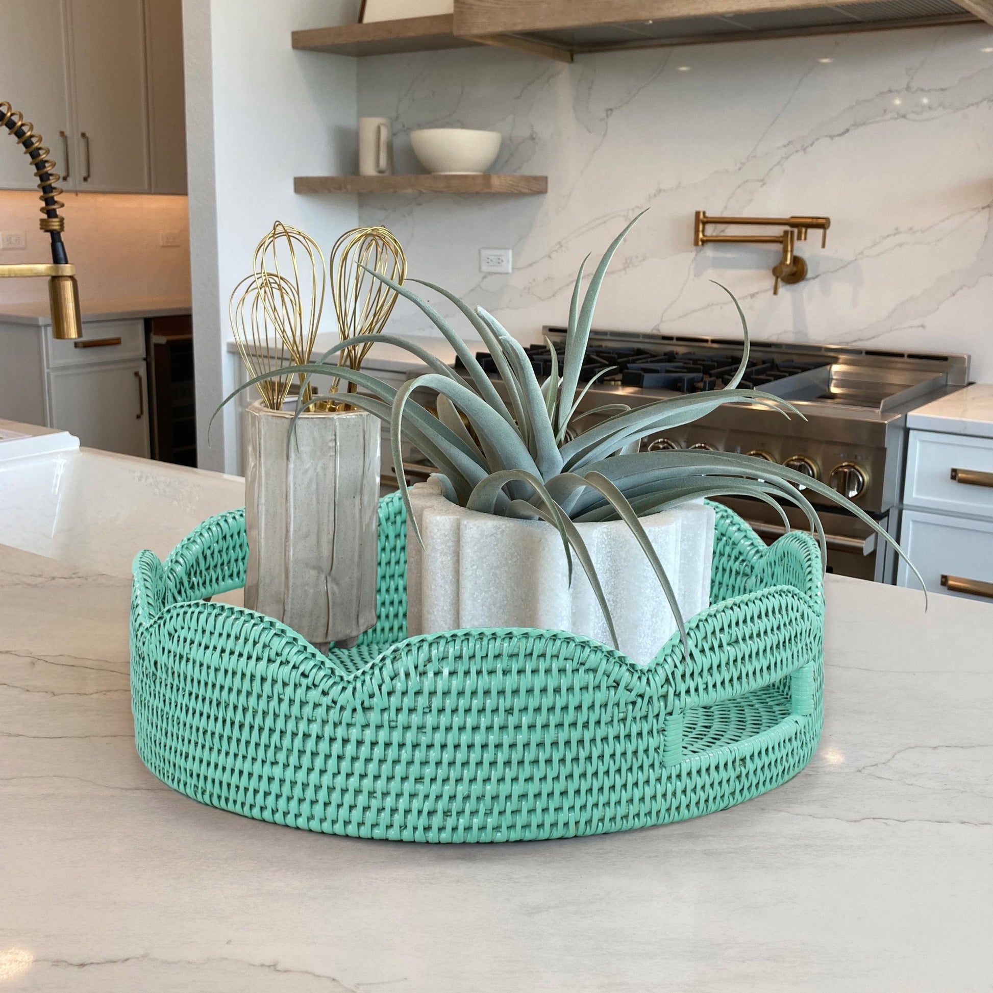 Sage leaf green scalloped round rattan tray styled on kitchen island with modern planters and greenery for fresh home decor.