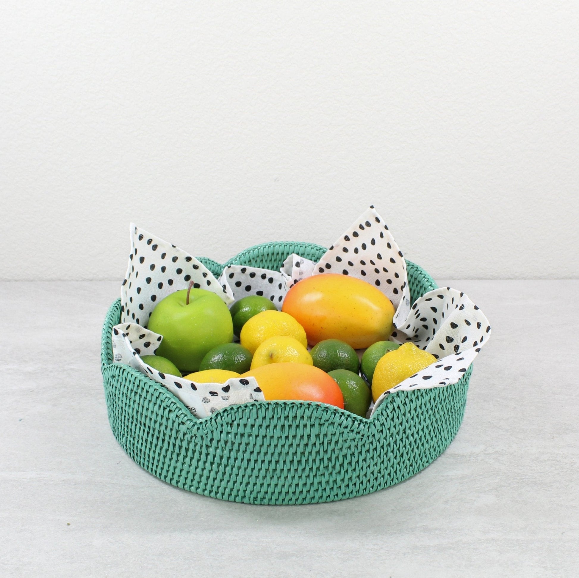 Turquoise scalloped round rattan tray with fresh fruit and dotted liner, styled as a decorative centerpiece or serving bowl.