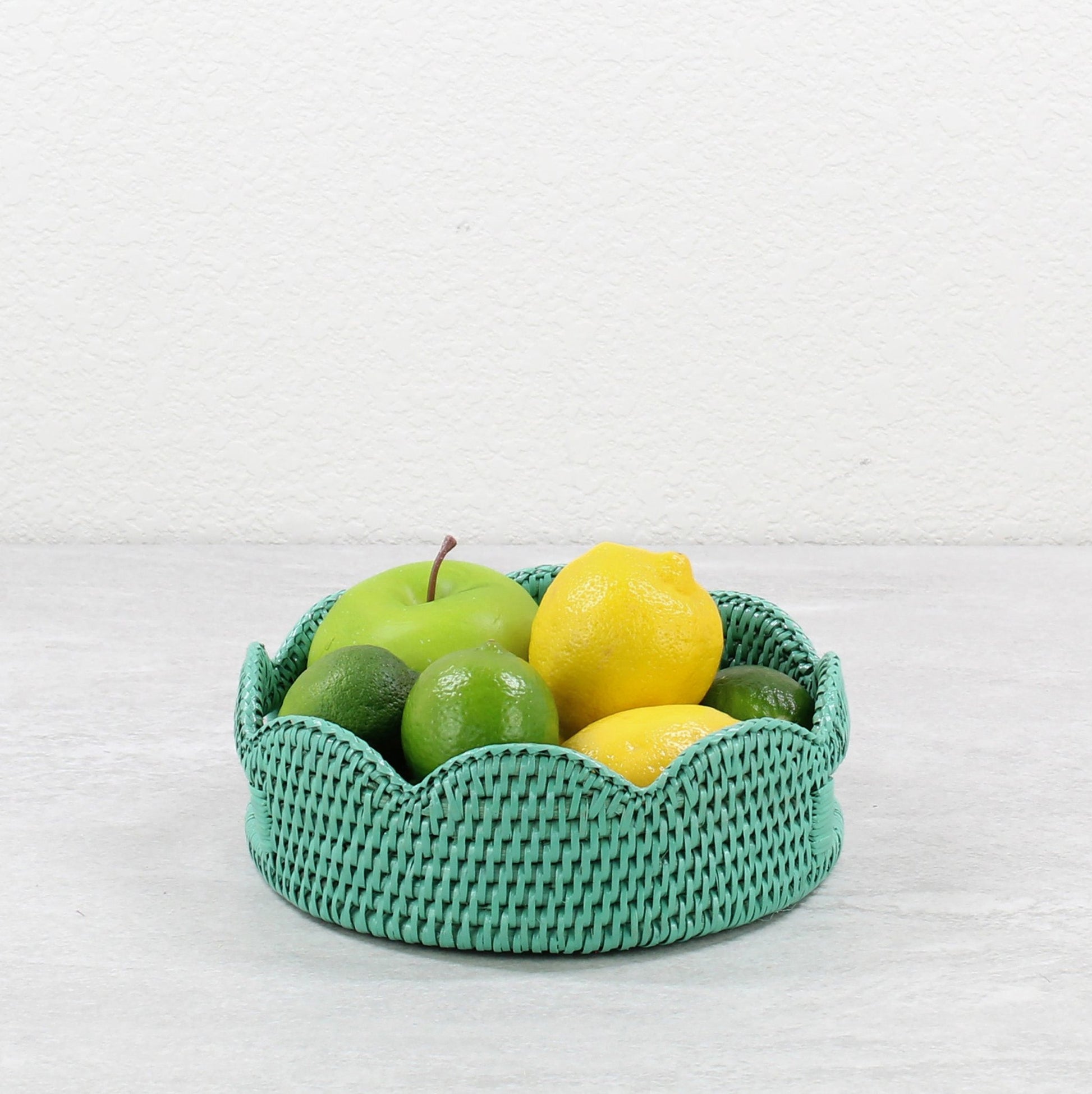 Small turquoise scalloped rattan tray with lemons, limes, and apple styled as a colorful fruit basket.