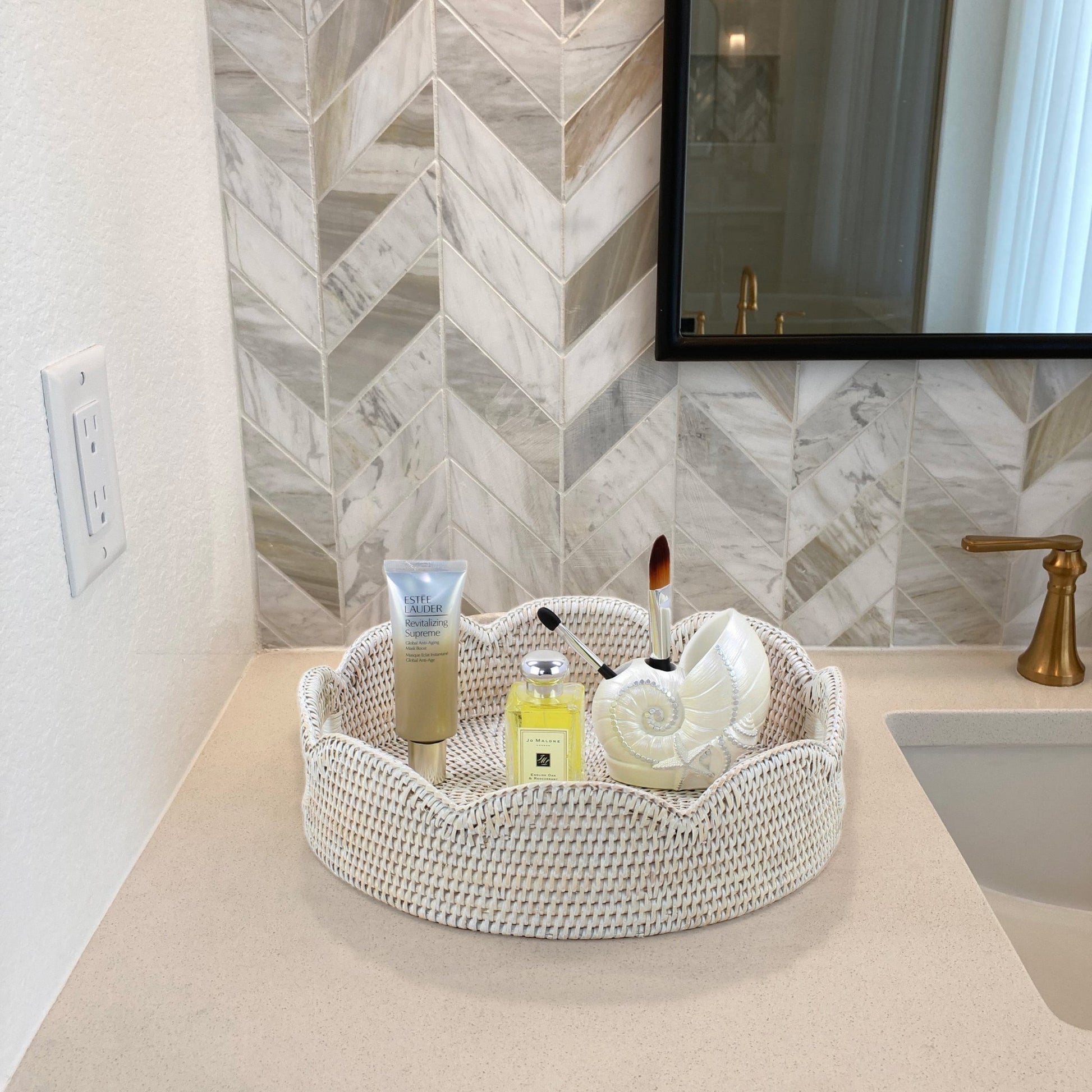 Whitewash scalloped round rattan tray on bathroom vanity holding Jo Malone perfume, Estée Lauder skincare, and seashell decor
