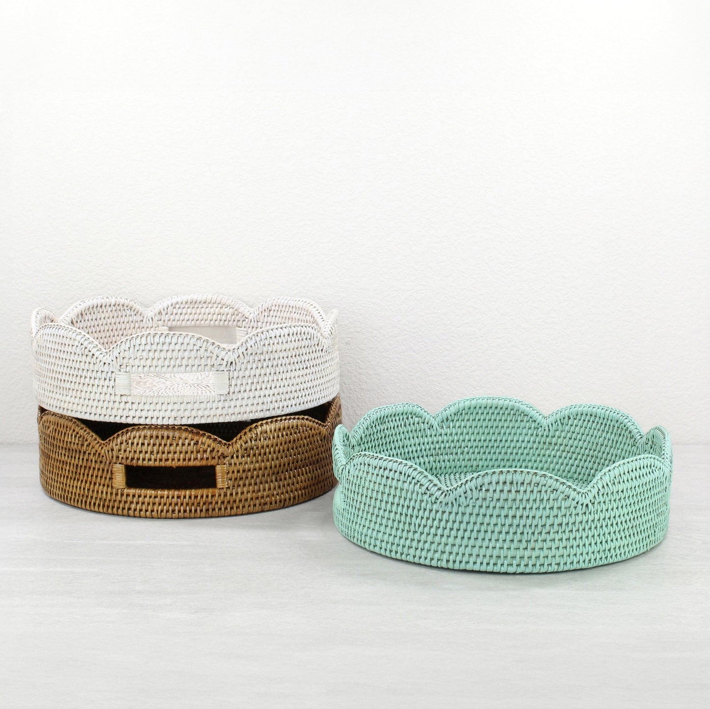 Eco Handcraft scalloped round rattan trays in whitewash, honey brown, andsage leaf green, stacked together as decorative storage baskets.