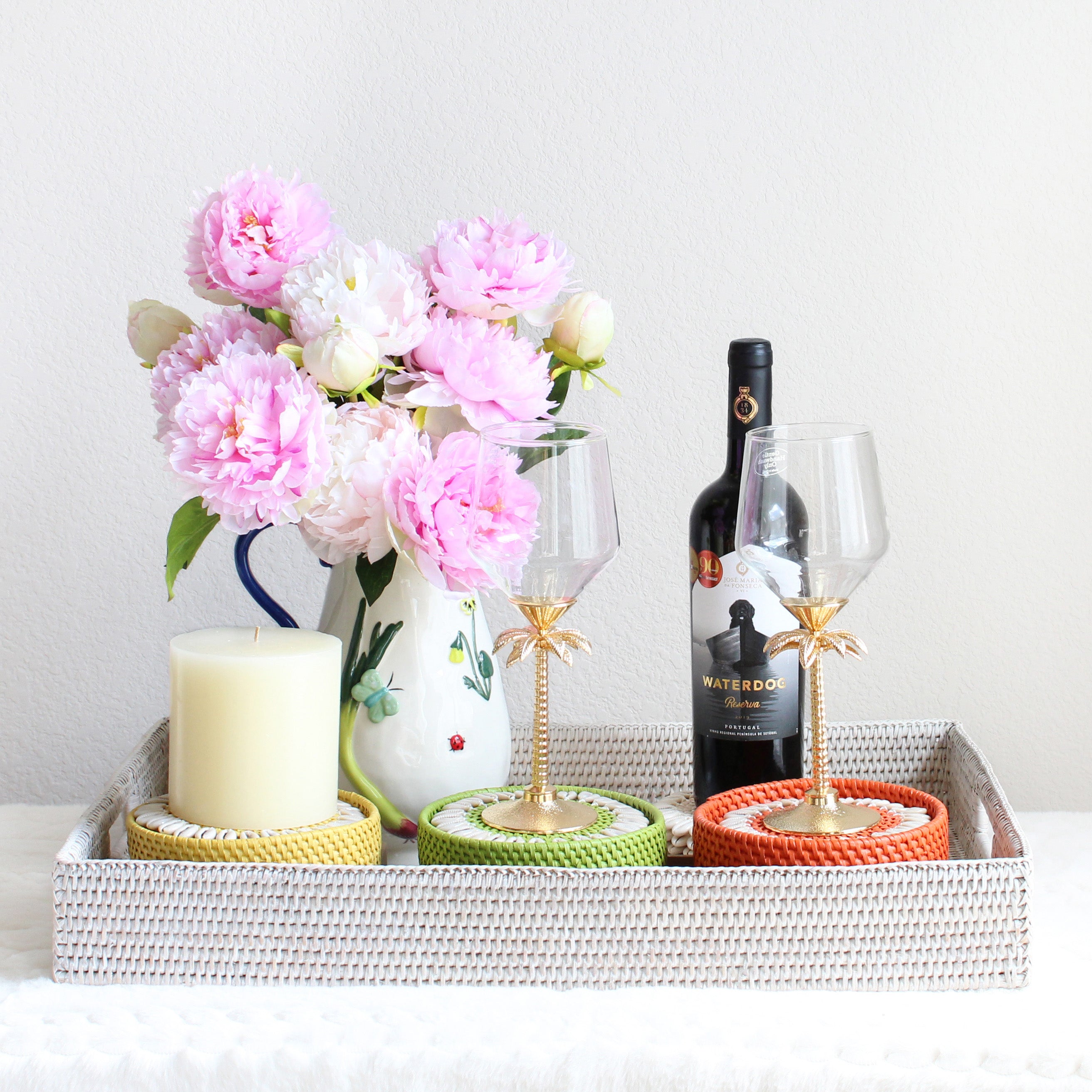 Anniversary gift set styled with handwoven whitewash rattan tray, seashell coasters, hand-painted stoneware picture, and floral pitcher with pink flowers